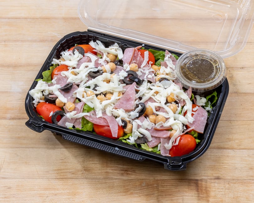 Antipasto salad with ham, salami, cheese, olives, chickpeas, and tomatoes in a to-go container.
