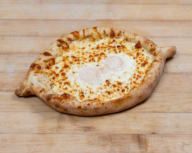 Adjaruli Khachapuri, a boat-shaped Georgian cheese bread with two baked eggs, on a wooden surface.