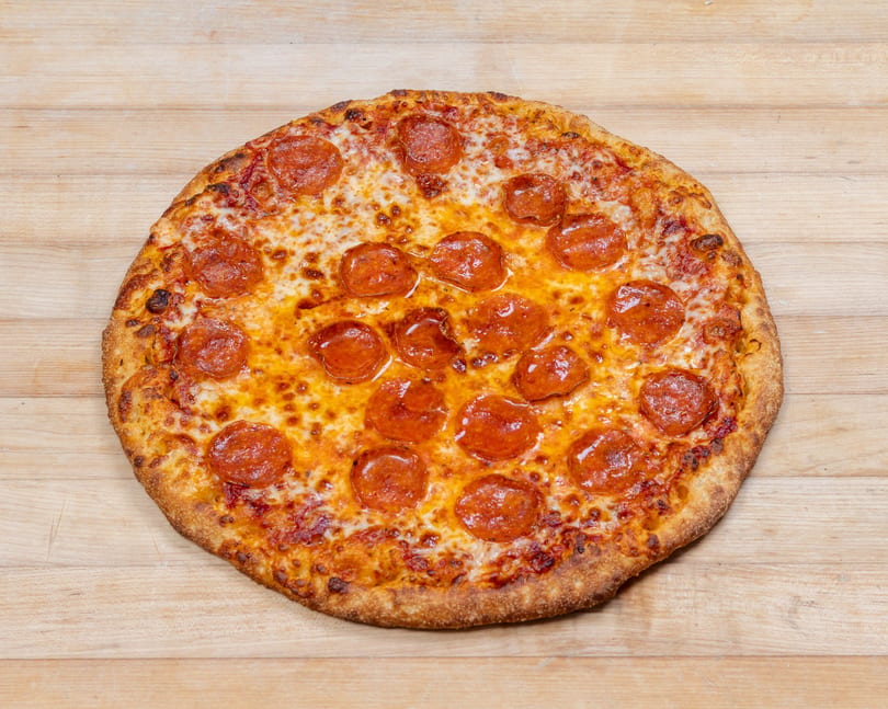 A whole pepperoni pizza with melted cheese and a golden crust on a light wooden surface.