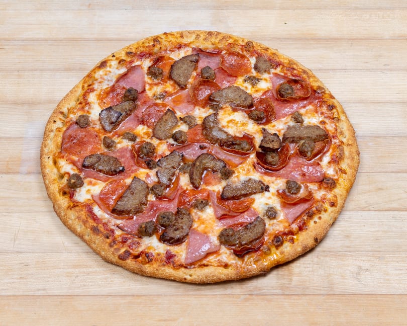 A whole meat lover's pizza with pepperoni, ham, and sausage on a wooden surface.