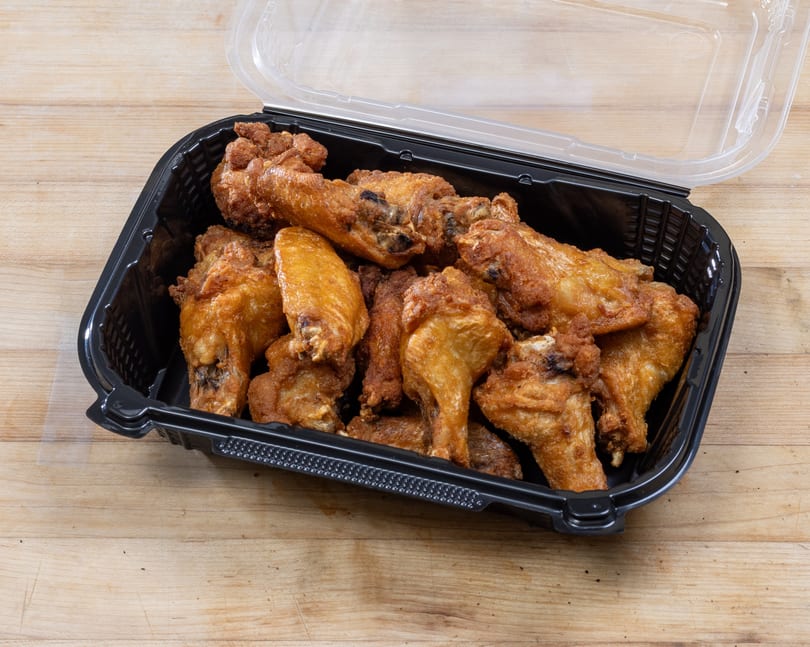 Crispy fried chicken wings and drumettes in a black plastic takeout container with a clear lid.