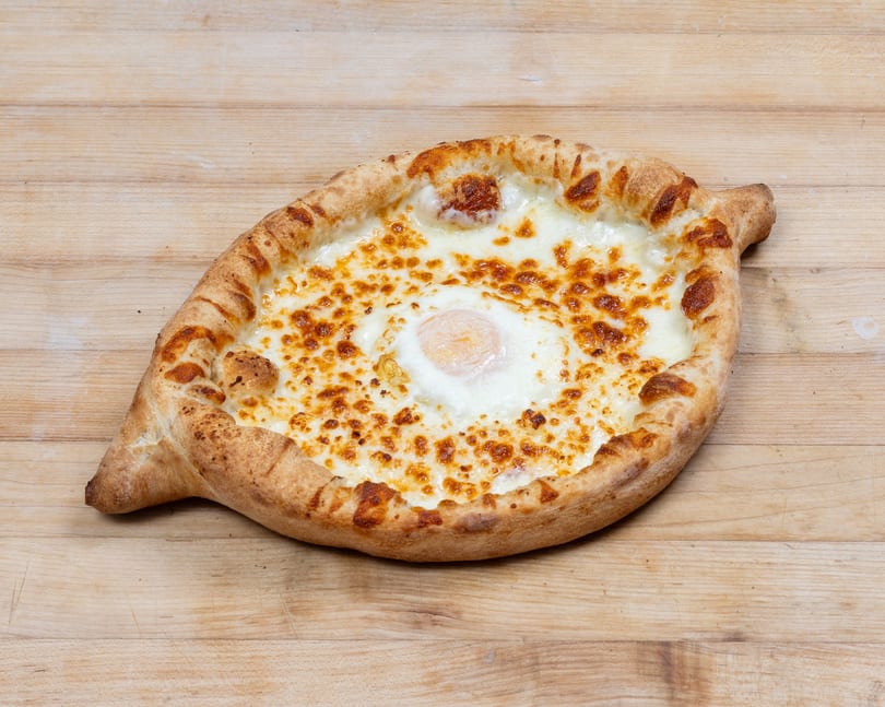 Adjaruli Khachapuri, a Georgian cheese bread boat with a baked egg in the center, on a wooden surface.