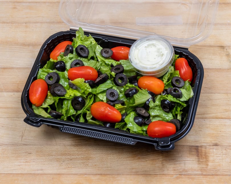 Fresh green salad with cherry tomatoes, black olives, and ranch dressing in a to-go container.